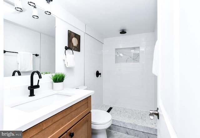 bathroom with tiled shower, vanity, and toilet