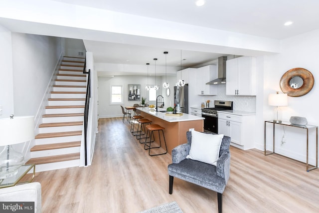 kitchen featuring stainless steel appliances, wall chimney range hood, a kitchen bar, a kitchen island with sink, and white cabinetry