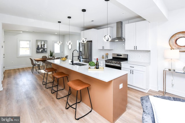 kitchen featuring a kitchen island with sink, stainless steel appliances, wall chimney exhaust hood, white cabinetry, and backsplash