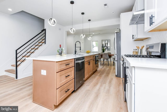 kitchen with a center island with sink, appliances with stainless steel finishes, hanging light fixtures, sink, and white cabinetry