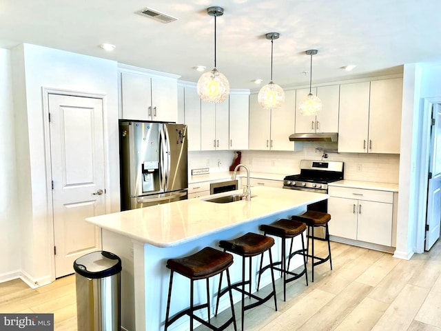 kitchen featuring appliances with stainless steel finishes, hanging light fixtures, an island with sink, sink, and white cabinetry