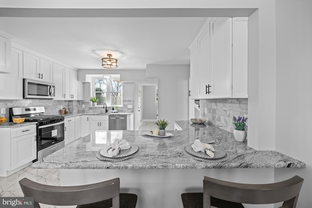 kitchen featuring white cabinetry, a kitchen bar, kitchen peninsula, and appliances with stainless steel finishes