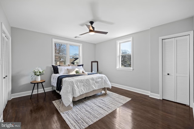 bedroom featuring ceiling fan, dark hardwood / wood-style floors, multiple closets, and multiple windows