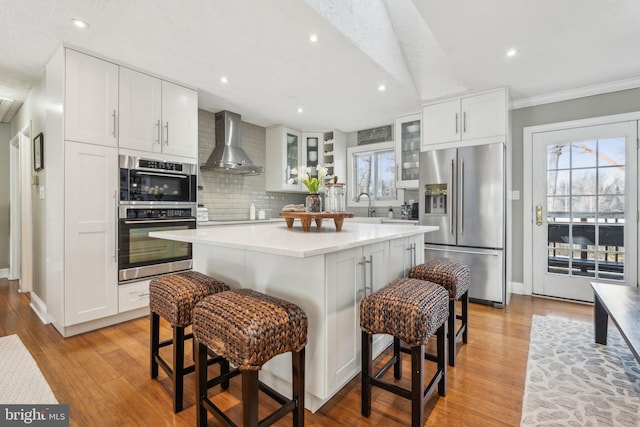 kitchen with wall chimney exhaust hood, appliances with stainless steel finishes, tasteful backsplash, a kitchen island, and white cabinetry