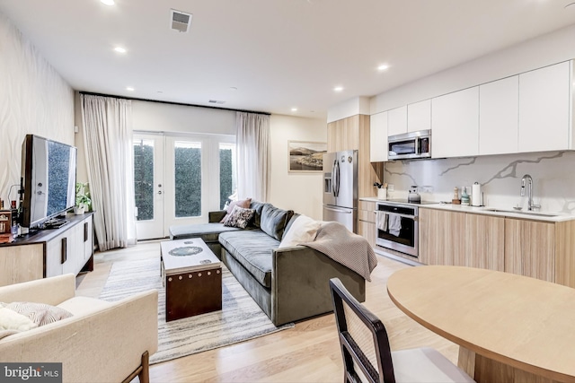 kitchen featuring appliances with stainless steel finishes, white cabinetry, french doors, tasteful backsplash, and sink