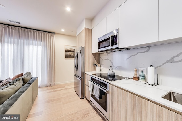 kitchen with tasteful backsplash, white cabinetry, light wood-type flooring, stainless steel appliances, and light stone counters