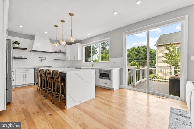 kitchen featuring premium range hood, white cabinetry, stainless steel appliances, backsplash, and a kitchen island