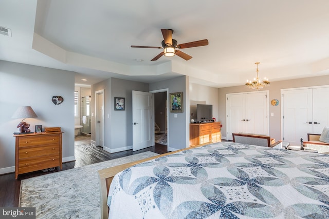 bedroom with ceiling fan with notable chandelier, two closets, connected bathroom, dark hardwood / wood-style floors, and a tray ceiling