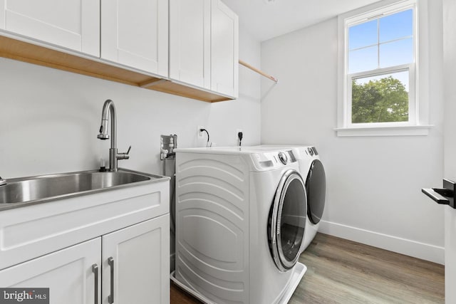 clothes washing area featuring cabinets, sink, light wood-type flooring, and washing machine and clothes dryer