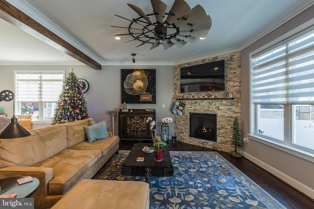 living room with a wealth of natural light, dark hardwood / wood-style flooring, crown molding, and a stone fireplace