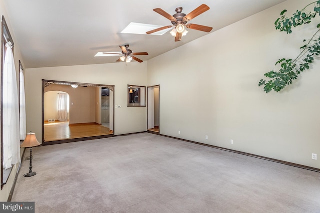 empty room with light carpet, vaulted ceiling with skylight, baseboards, arched walkways, and a ceiling fan