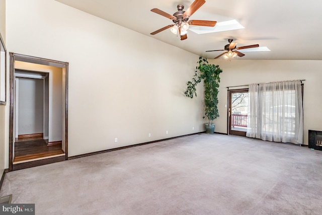 carpeted spare room with lofted ceiling with skylight, baseboards, and a ceiling fan