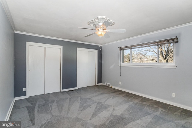 unfurnished bedroom with ornamental molding, carpet, visible vents, and two closets