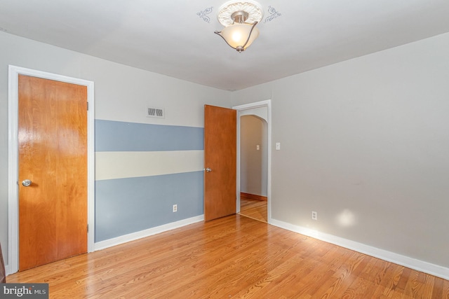 unfurnished room with baseboards, visible vents, arched walkways, and wood finished floors