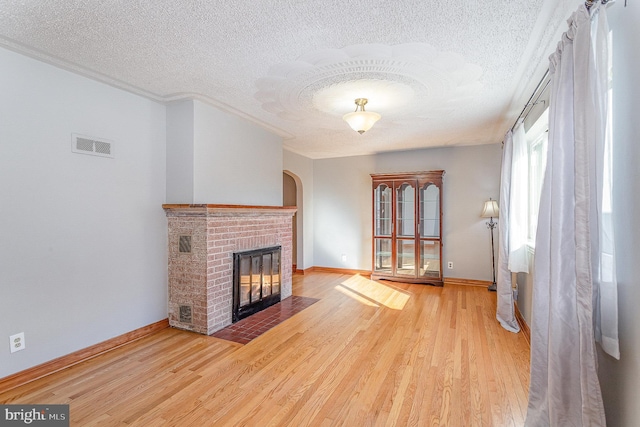 unfurnished living room featuring visible vents, a fireplace, a textured ceiling, and wood finished floors