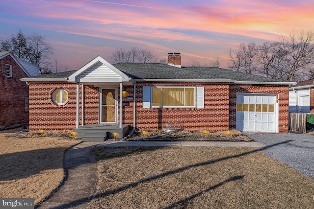 ranch-style house featuring an attached garage, driveway, a chimney, and brick siding