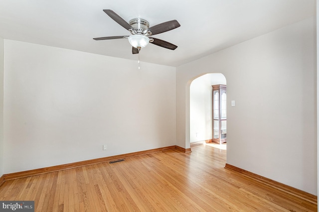 spare room with light wood-style floors, arched walkways, visible vents, and baseboards