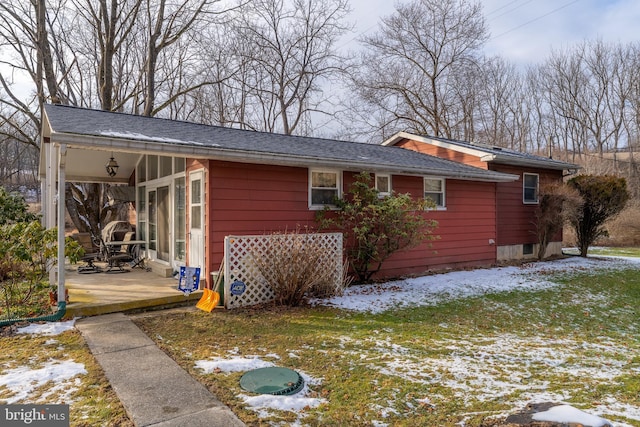 snow covered back of property featuring a patio and a yard