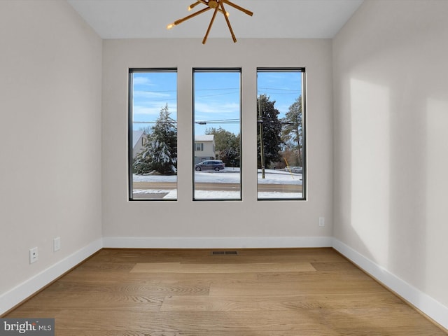 spare room with an inviting chandelier, light wood-type flooring, and a wealth of natural light