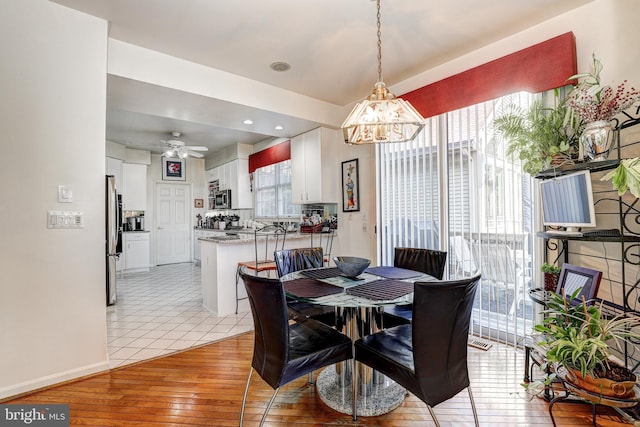 dining space with ceiling fan with notable chandelier and light wood-type flooring