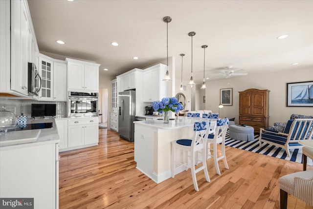 kitchen featuring tasteful backsplash, white cabinetry, hanging light fixtures, a kitchen island with sink, and appliances with stainless steel finishes