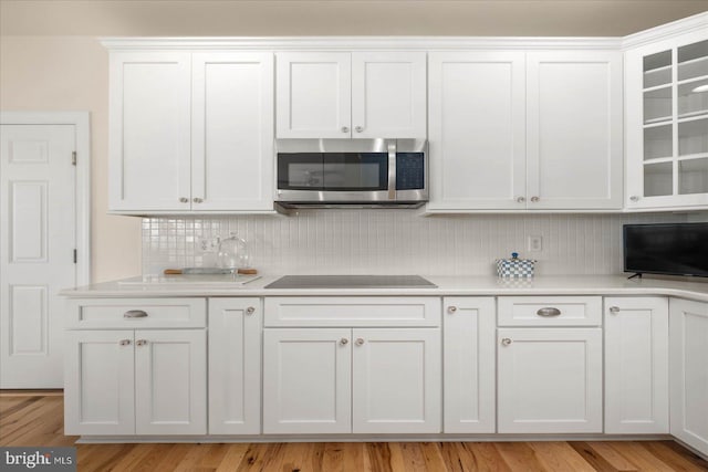 kitchen featuring black electric cooktop, backsplash, white cabinets, and light wood-type flooring