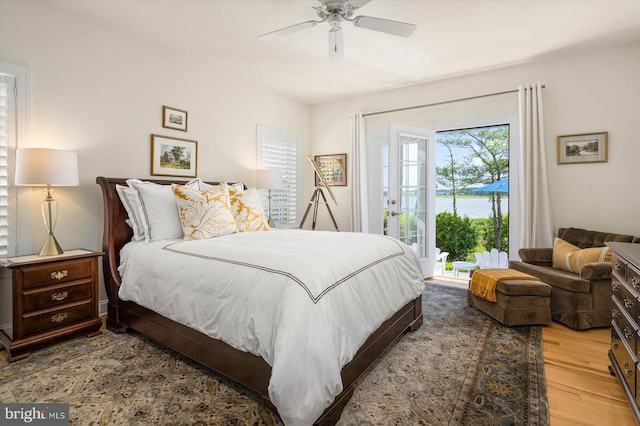 bedroom featuring ceiling fan, access to exterior, wood-type flooring, and a water view