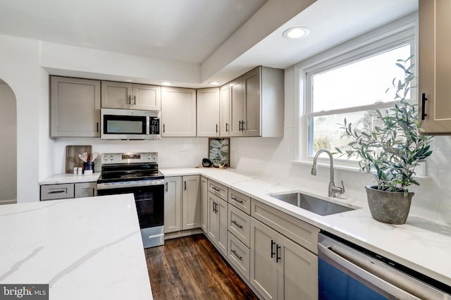 kitchen featuring stainless steel appliances, sink, light stone counters, dark hardwood / wood-style floors, and gray cabinetry