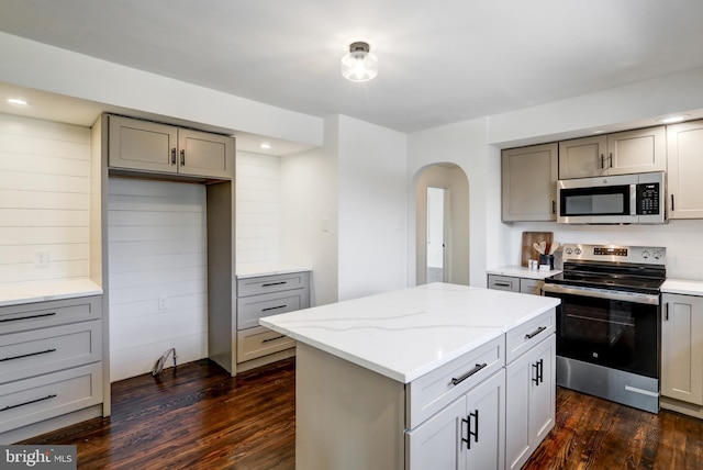 kitchen with a center island, light stone counters, gray cabinets, dark hardwood / wood-style flooring, and appliances with stainless steel finishes