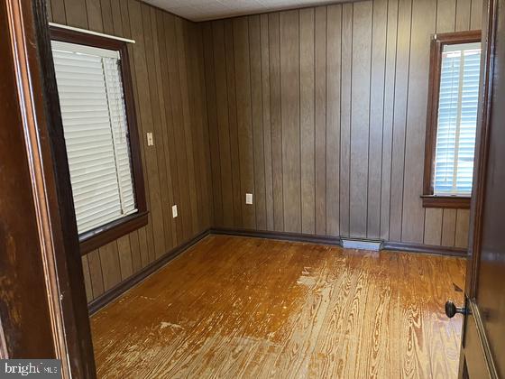 spare room with hardwood / wood-style flooring, wood walls, and a healthy amount of sunlight