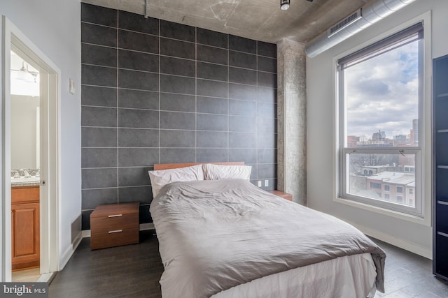 bedroom featuring dark wood-type flooring, multiple windows, ensuite bath, and tile walls