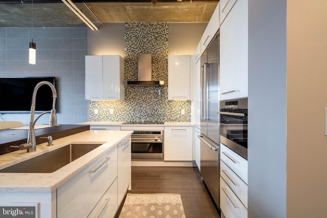 kitchen featuring wall chimney exhaust hood, appliances with stainless steel finishes, sink, and white cabinets