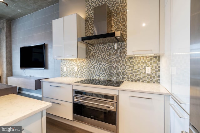 kitchen with dark wood-type flooring, wall chimney exhaust hood, black electric stovetop, oven, and white cabinets