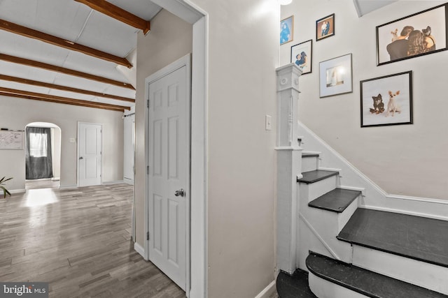 staircase featuring wood-type flooring and lofted ceiling with beams