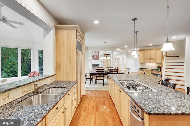 kitchen with dark stone counters, hanging light fixtures, light wood-type flooring, and a sink