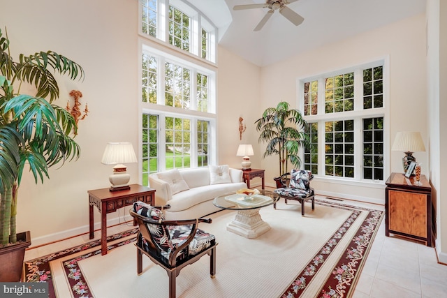 living room with ceiling fan, a towering ceiling, baseboards, and light tile patterned floors