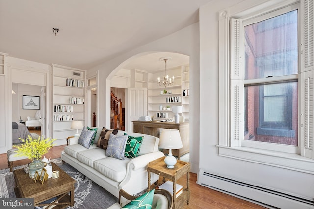 living room featuring wood-type flooring, a baseboard heating unit, built in features, and an inviting chandelier