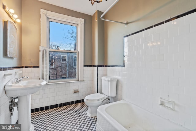 bathroom featuring a washtub, tile walls, toilet, and sink