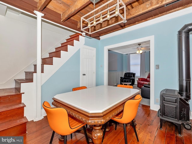 dining space with wood ceiling, wood-type flooring, beamed ceiling, ceiling fan, and a wood stove