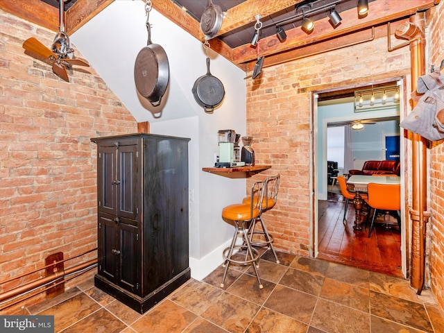 kitchen with ceiling fan, beamed ceiling, and brick wall