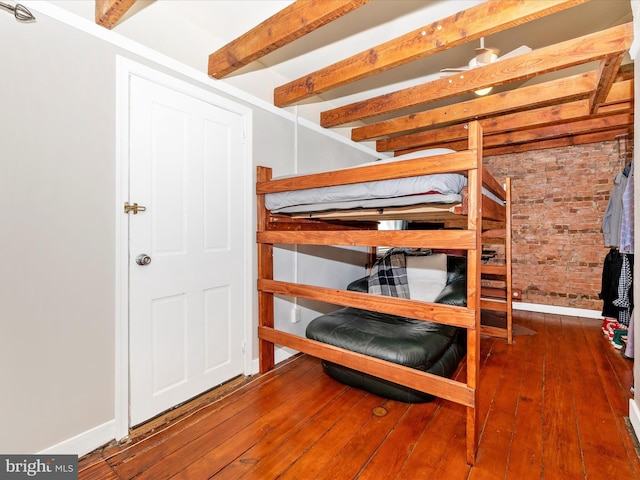 unfurnished bedroom with beam ceiling, hardwood / wood-style floors, and brick wall