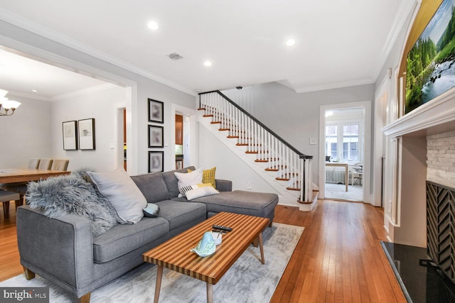 living room featuring an inviting chandelier, a stone fireplace, ornamental molding, and light hardwood / wood-style floors