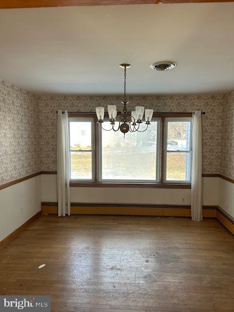 unfurnished dining area with a baseboard heating unit, hardwood / wood-style floors, and a chandelier