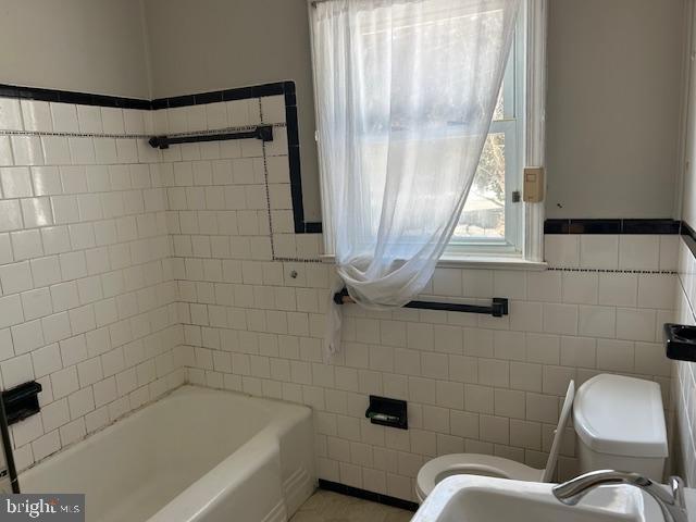 bathroom with a tub to relax in, toilet, sink, and tile walls