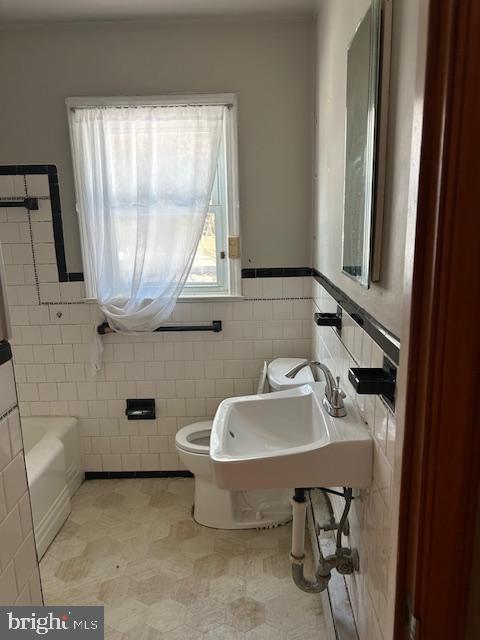 bathroom featuring a tub to relax in, toilet, sink, and tile walls