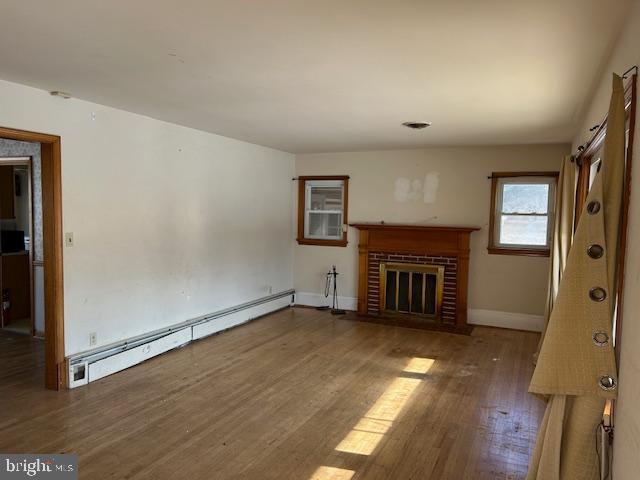 unfurnished living room with a brick fireplace, hardwood / wood-style flooring, and baseboard heating