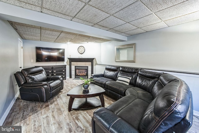 living room featuring hardwood / wood-style floors, a tile fireplace, and a drop ceiling