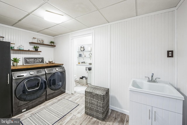 washroom featuring sink, wooden walls, cabinets, separate washer and dryer, and light hardwood / wood-style flooring