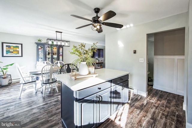 kitchen with ceiling fan with notable chandelier, a center island, pendant lighting, and dark wood-type flooring