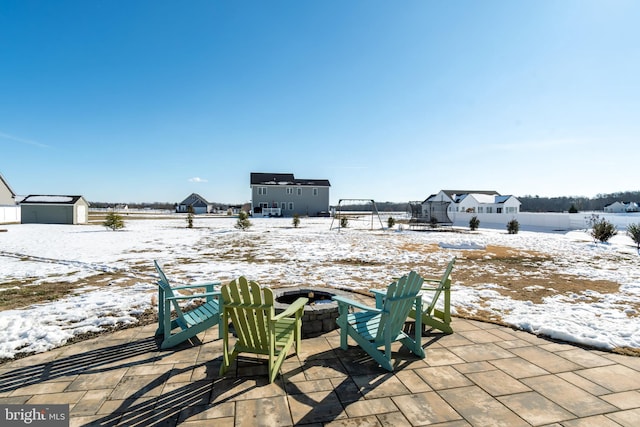 snow covered patio featuring a storage shed, a trampoline, and a fire pit